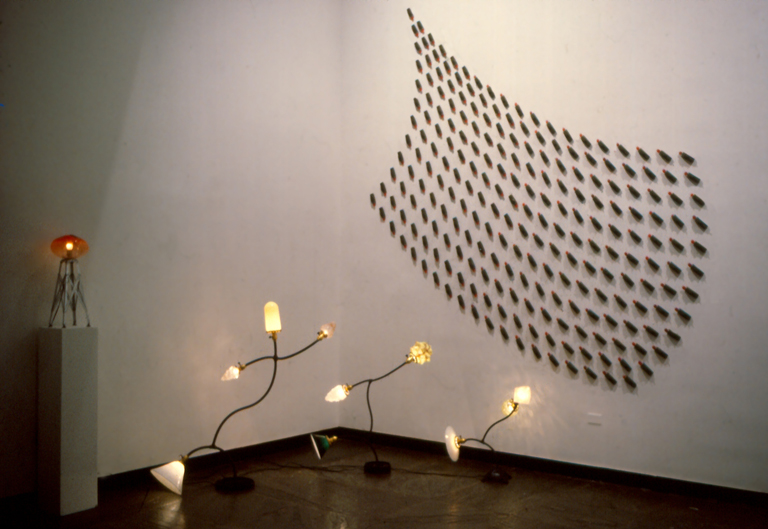 Photograph of Harry Andersons art work in the 1981 exhibit Made in Philadelphia 4 at the ICA showing four of Andersons lamps and a wall installation made of toy tanks